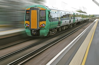 Green and yellow commuter train speeding past station platform