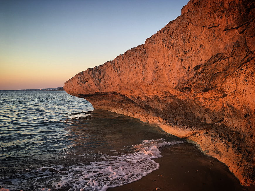 Sunlit Red Rock Cliff Overlooking Calm Ocean Waves