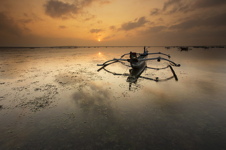Traditional outrigger boat on calm sea at golden sunset