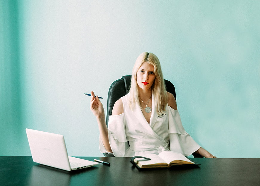 Blonde Businesswoman Sitting At Desk With Laptop And Notebook