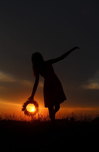Silhouette of woman holding flower wreath at sunset in field