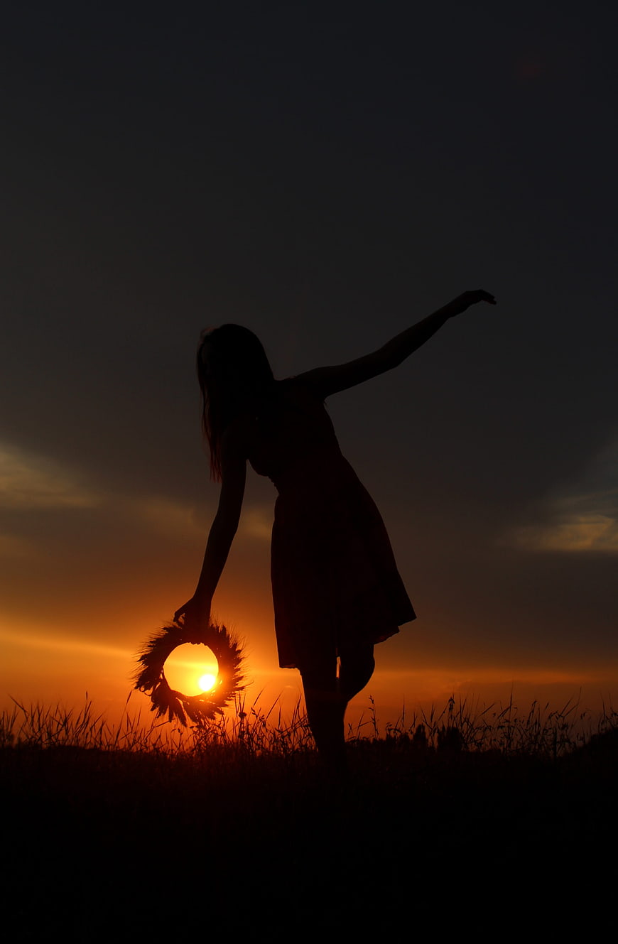 Silhouette of woman holding flower wreath at sunset in field