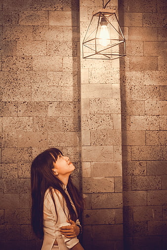 Woman looking up at geometric pendant light against stone wall