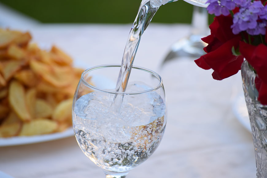 Pouring Sparkling Water Into Glass With Chips And Flowers
