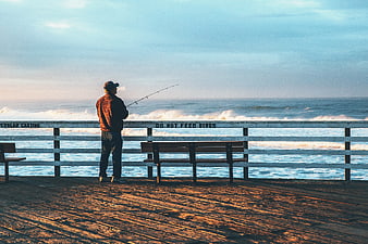Man fishing on wooden pier at sunset