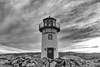 Black and white lighthouse on rocky hill with dramatic clouds
