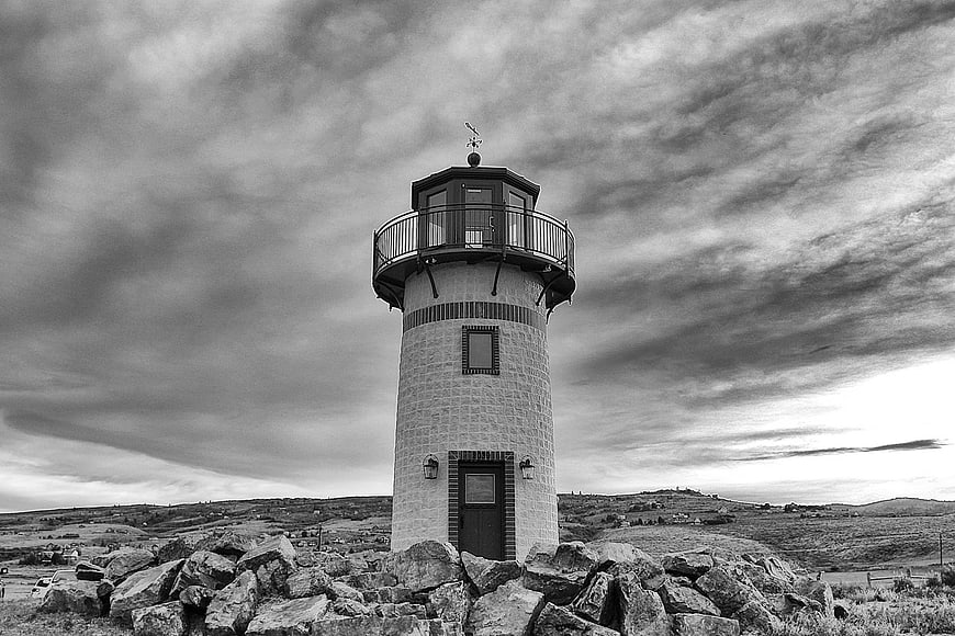 Black and white lighthouse on rocky hill with dramatic clouds