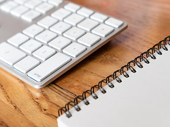 White Keyboard and Spiral Notebook on Wooden Desk