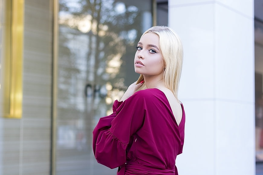 Blonde Woman In Burgundy Dress Standing In Urban Setting