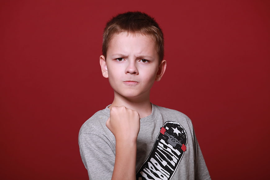 Angry young boy with clenched fist on red background