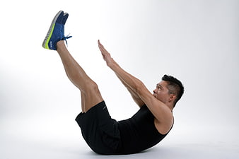 Athletic man performing V-sit exercise in studio