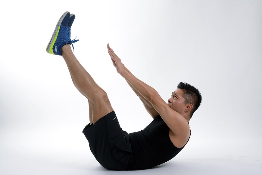 Athletic man performing V-sit exercise in studio