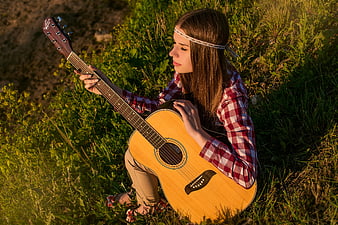 Young woman playing acoustic guitar in grassy field at sunset