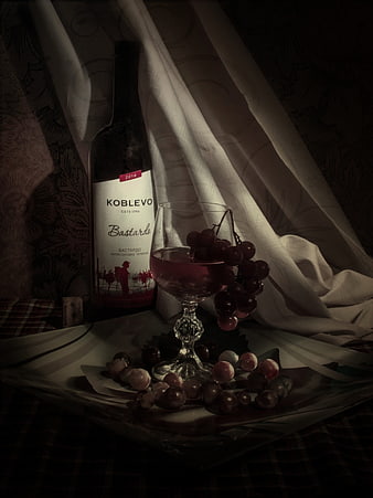 Dark moody still life of wine bottle, glass, and grapes