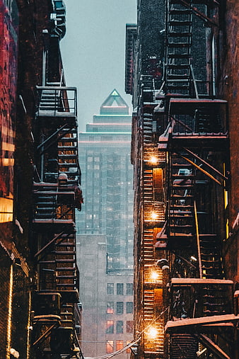 Snowy urban alley with fire escapes and city skyline