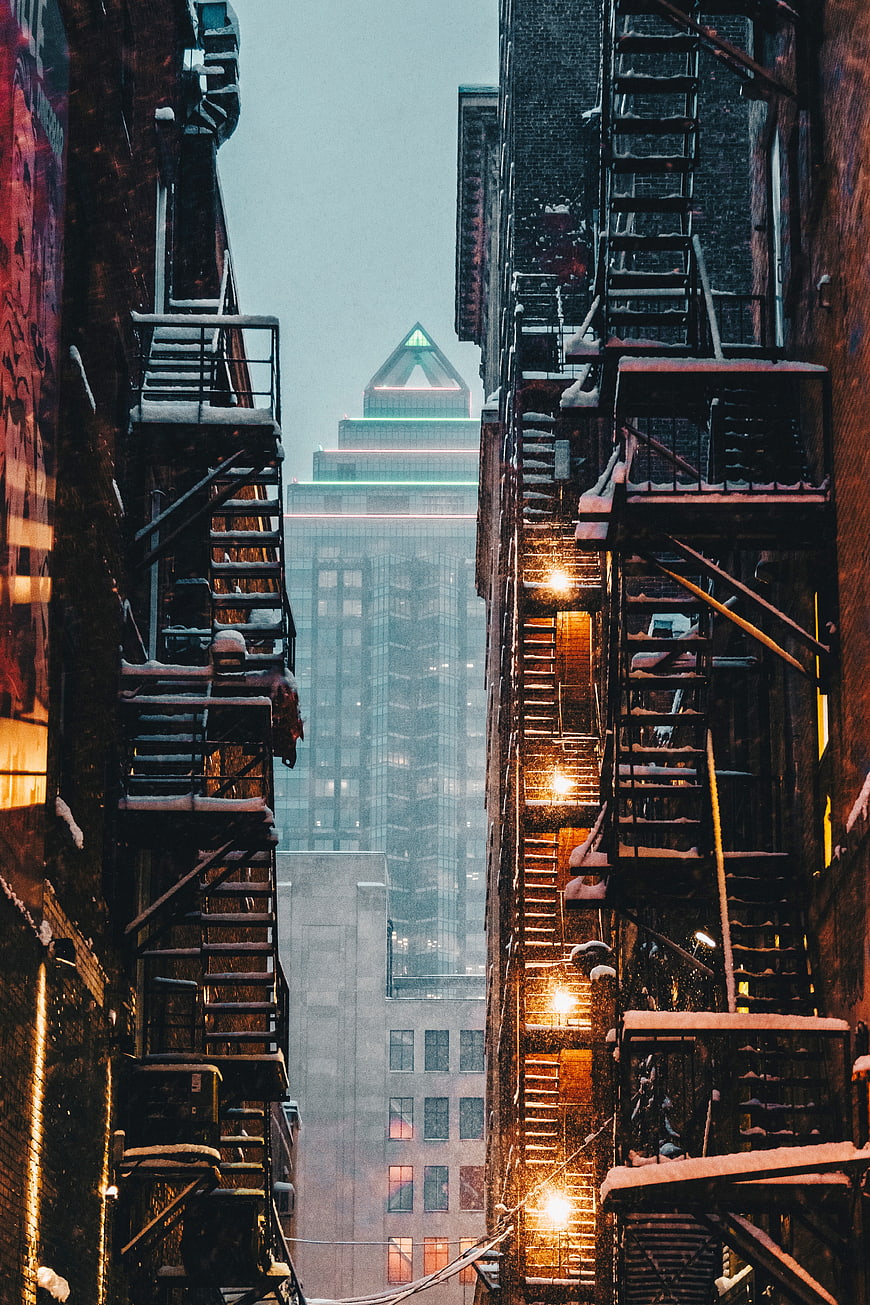 Snowy urban alley with fire escapes and city skyline