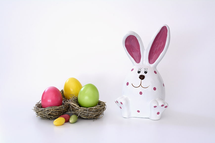 White ceramic Easter bunny figurine with colorful eggs in twigs nest