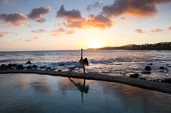 Woman doing yoga pose on ocean pier at sunset