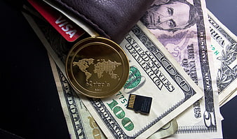 Ripple coin, US dollar bills, Visa card, and wallet on dark background