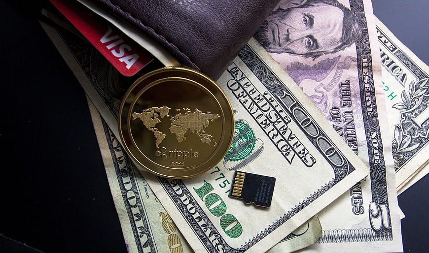 Ripple coin, US dollar bills, Visa card, and wallet on dark background