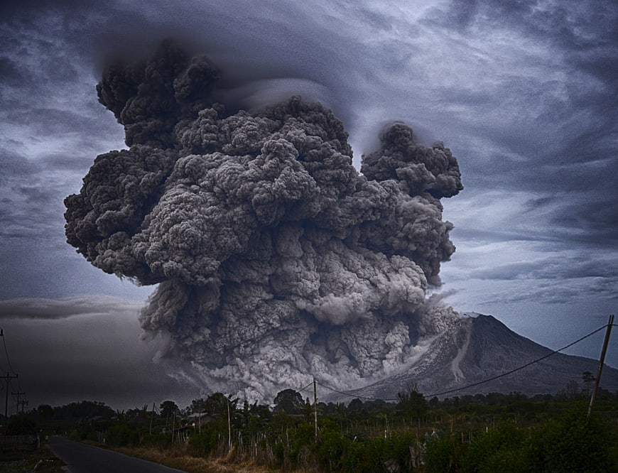 Massive volcanic eruption plume rising over rural landscape