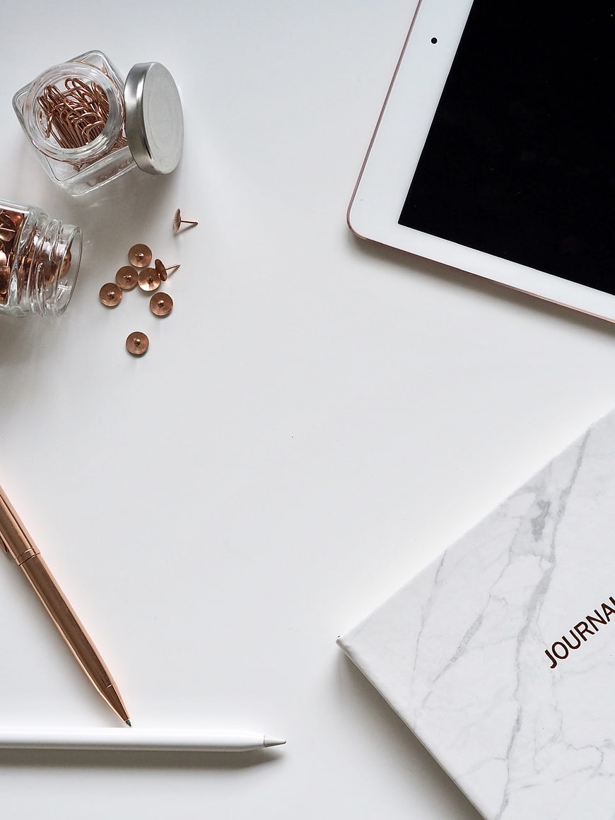 Minimalist white desk flat lay with tablet, journal, and rose gold stationery