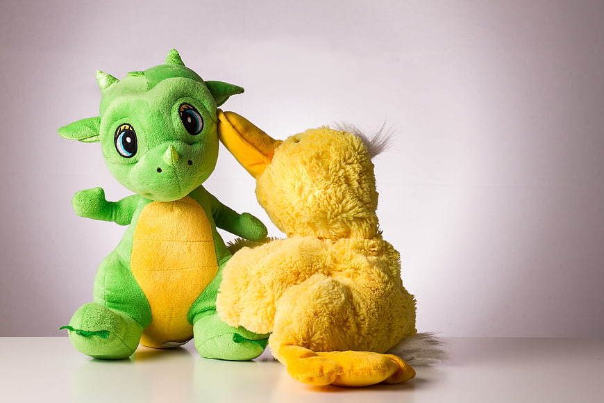 Green Dragon and Yellow Duck Plush Toys Interacting on White Background