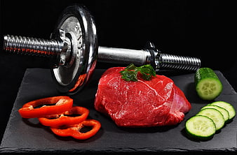 Raw beef steak with dumbbell, cucumber, and red pepper on dark slate
