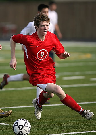 Young Male Soccer Player Dribbling Ball in Red Jersey