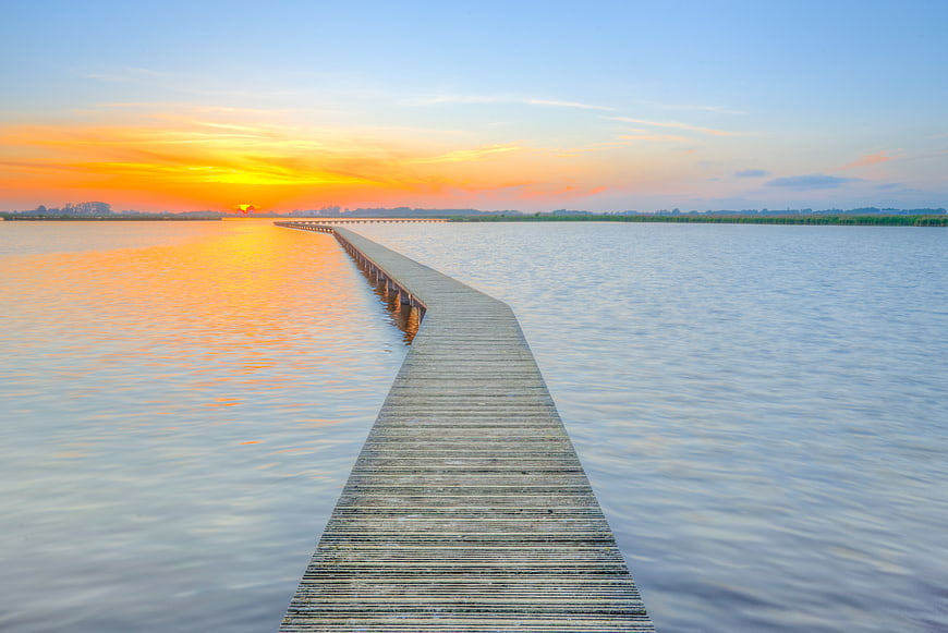 Wooden pier extending into calm lake at vibrant sunset
