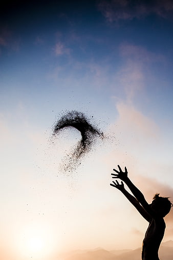 Silhouette of a child throwing sand into the sunset sky
