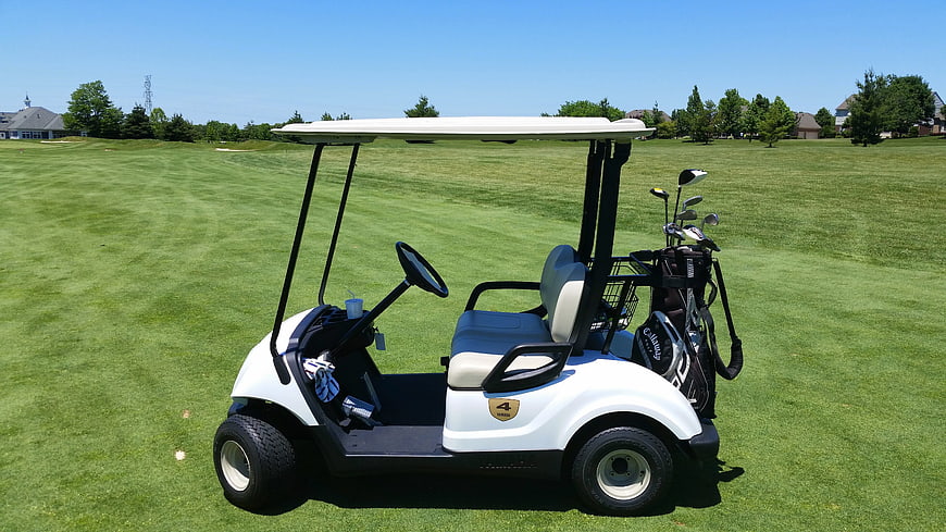 White golf cart with clubs on a sunny green golf course