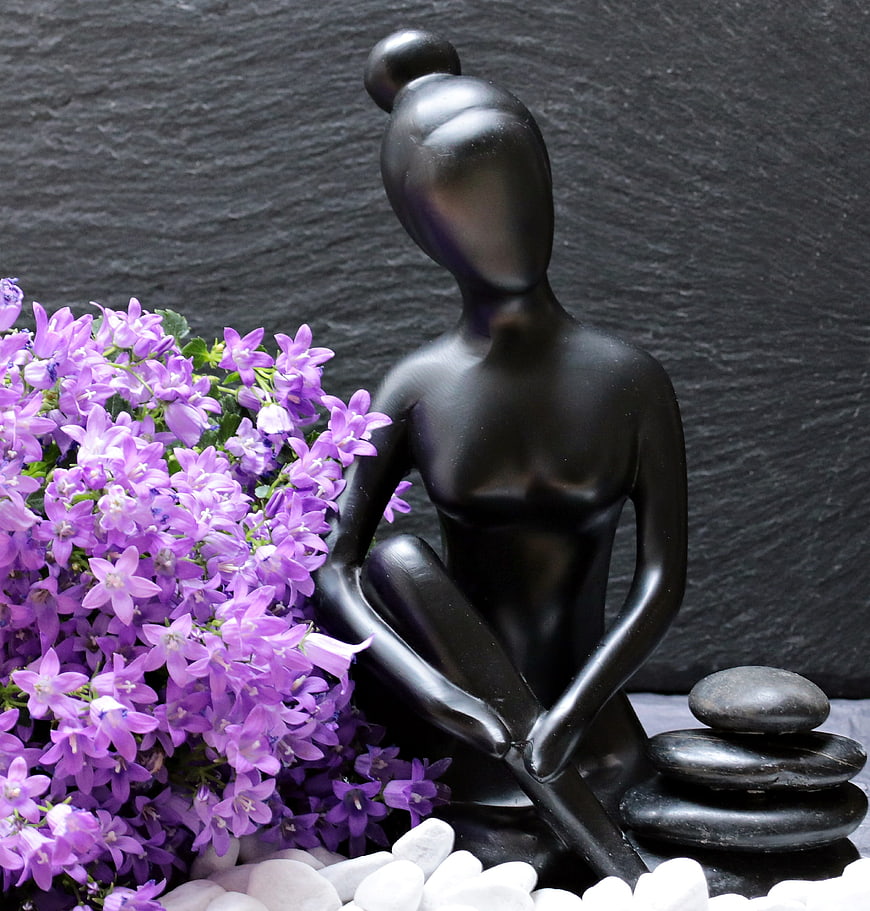Black female sculpture in meditation pose with purple flowers and zen stones