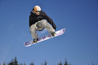 Snowboarder performing mid-air jump against clear blue winter sky