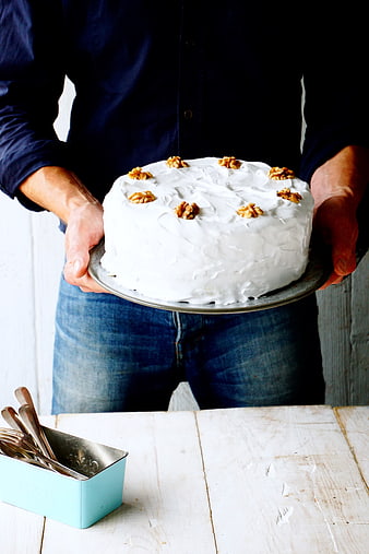 Man holding white frosted cake with walnuts on rustic table