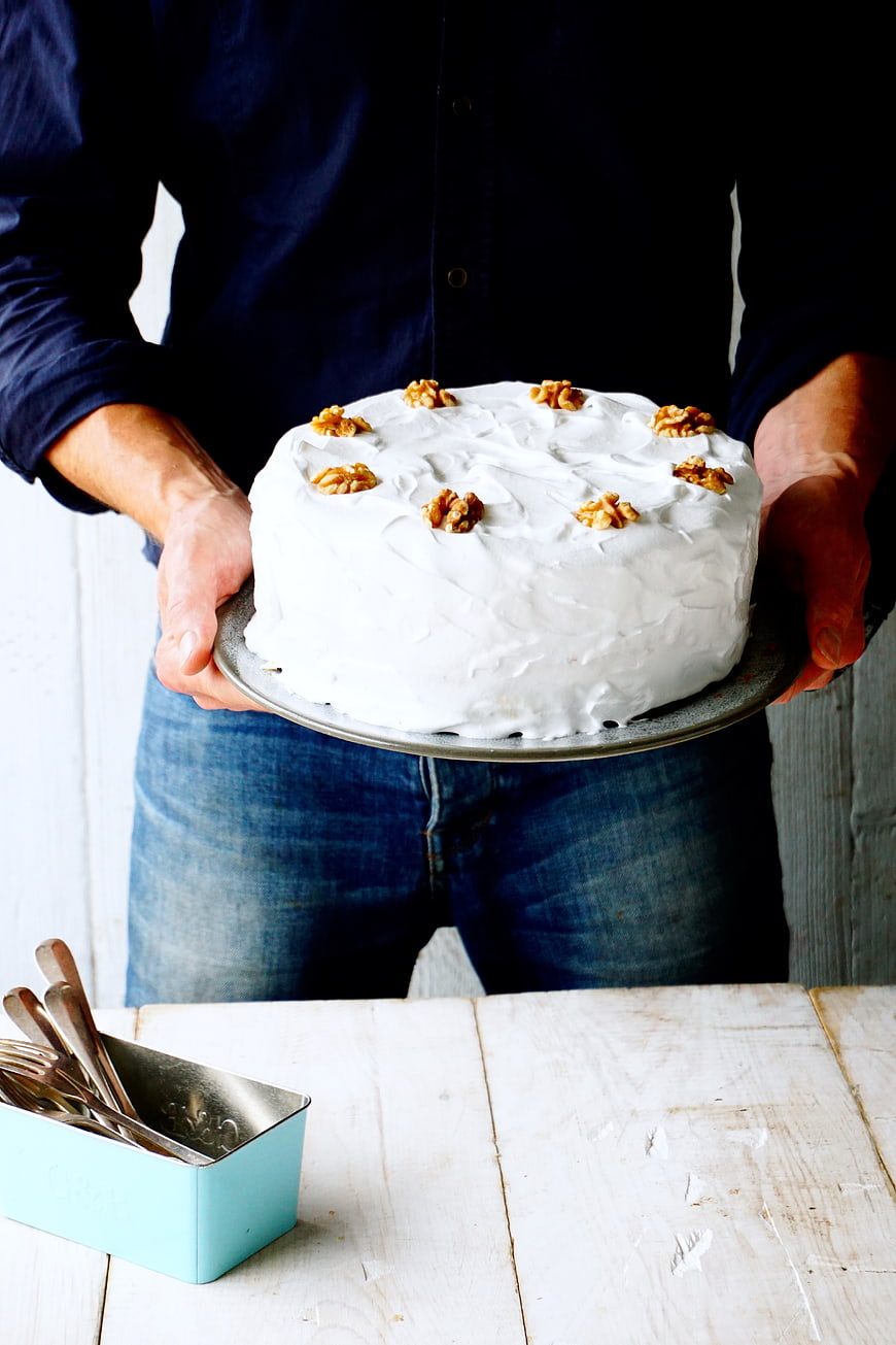 Man holding white frosted cake with walnuts on rustic table