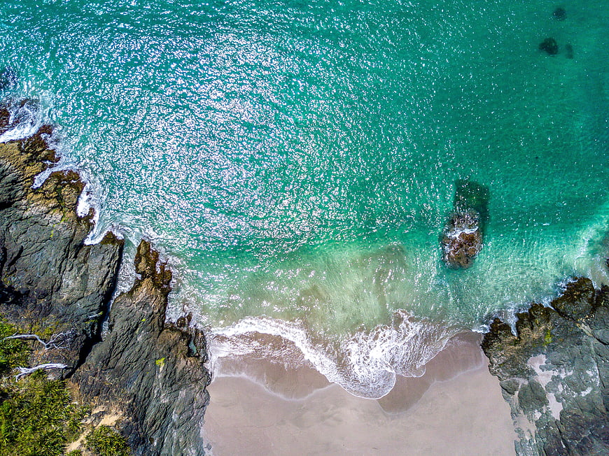 Aerial View of Turquoise Ocean Waves Crashing on Rocky Beach
