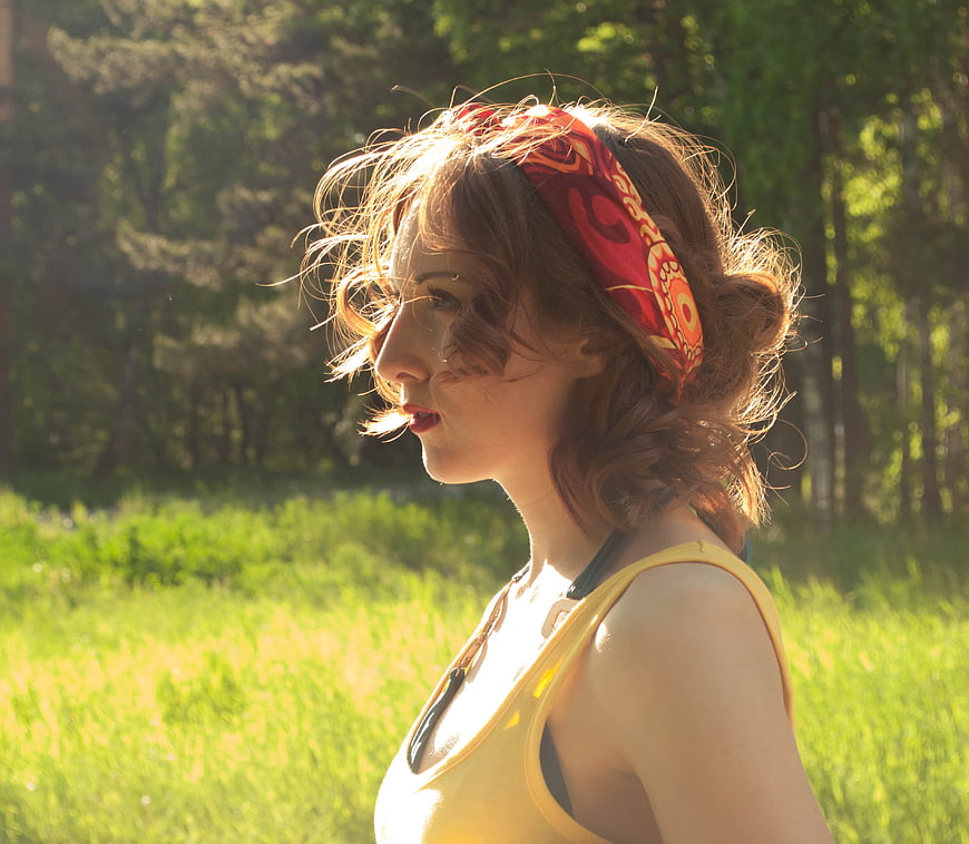 Redhead woman in yellow tank top and red headband in sunny summer field