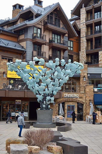 Modern blue glass sculpture in outdoor plaza with mountain architecture
