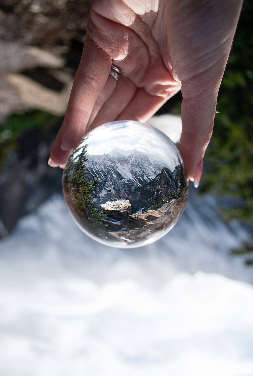 Hand holding crystal ball reflecting snowy mountain landscape