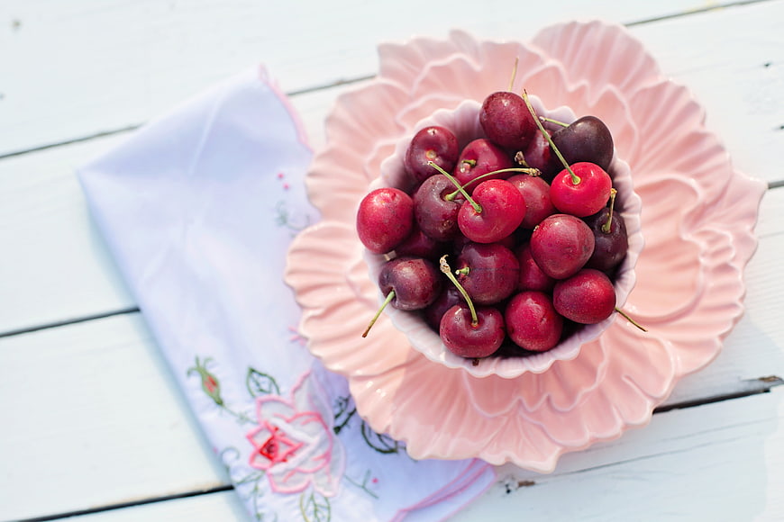 Fresh red cherries in a pink flower-shaped ceramic bowl