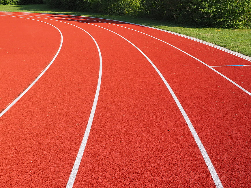 Red running track with white lane lines curving through a stadium