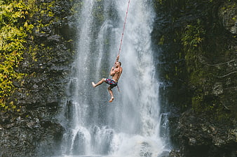 Man swinging on rope in front of tropical waterfall