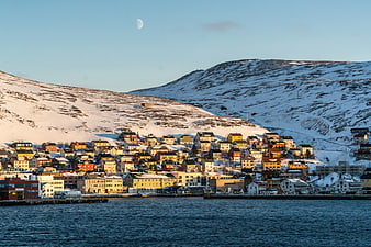 Colorful coastal town on snowy mountain slope with moon