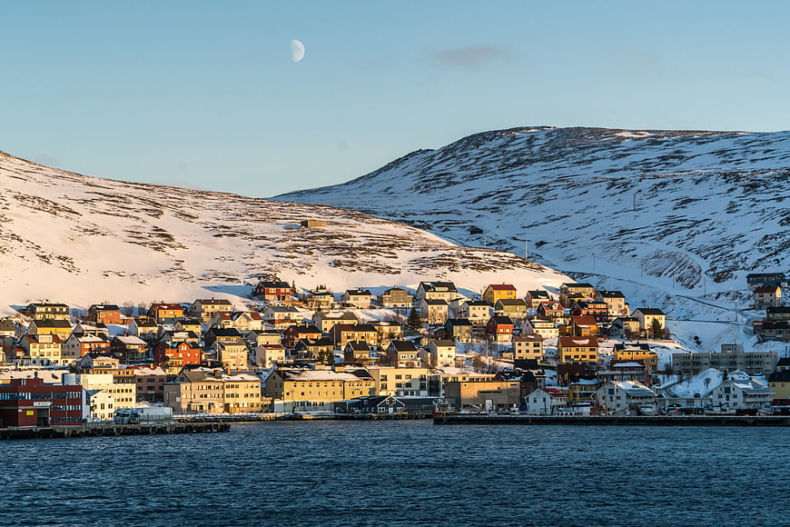 Colorful coastal town on snowy mountain slope with moon