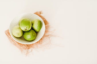 Fresh green limes in a white ceramic bowl on a white background