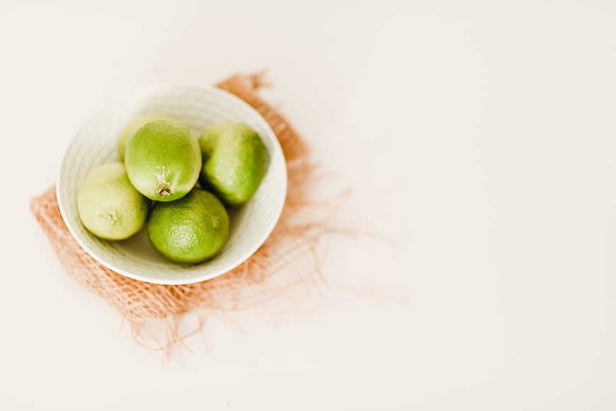 Fresh green limes in a white ceramic bowl on a white background