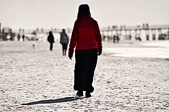 Woman in Red Jacket Walking on Sandy Beach