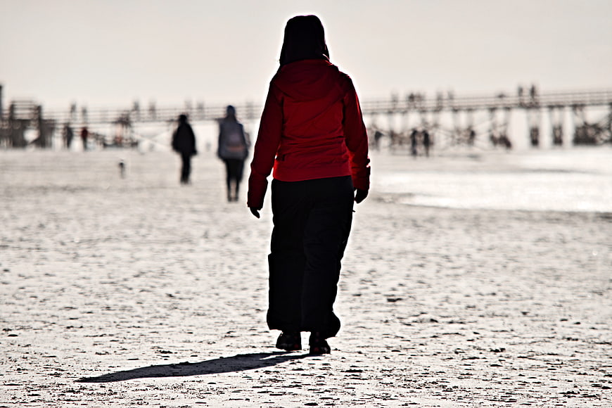 Woman in Red Jacket Walking on Sandy Beach