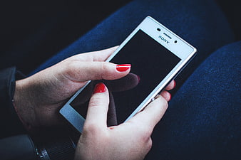 Woman with red nails holding white smartphone on blue jeans